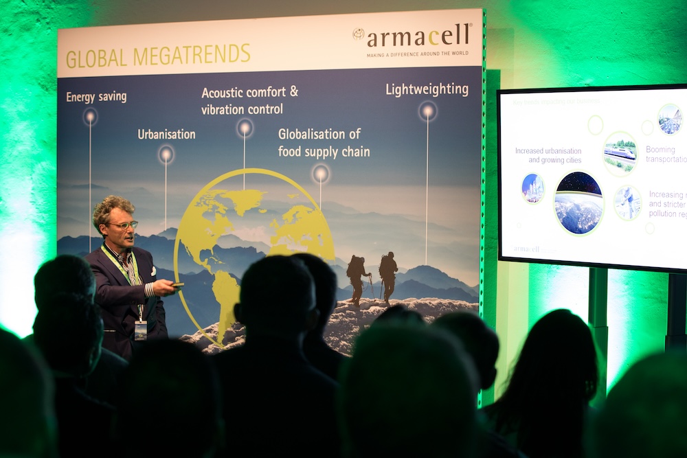 Speakers at the Armacell Armarium Days, featuring graphic event displays A speaker addressing the audience at the Armacell Armarium Days management conference, featuring large-format graphic displays and a presentation area.