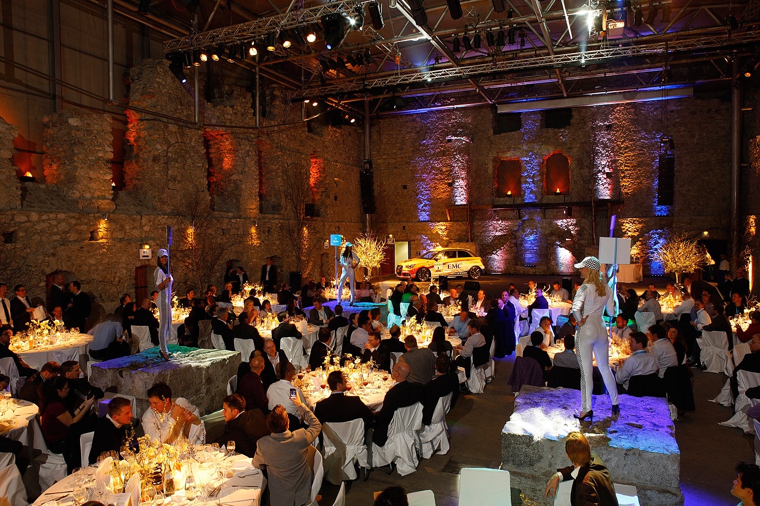 A festively decorated event hall with attendees and a stage at the EMC Partner Event