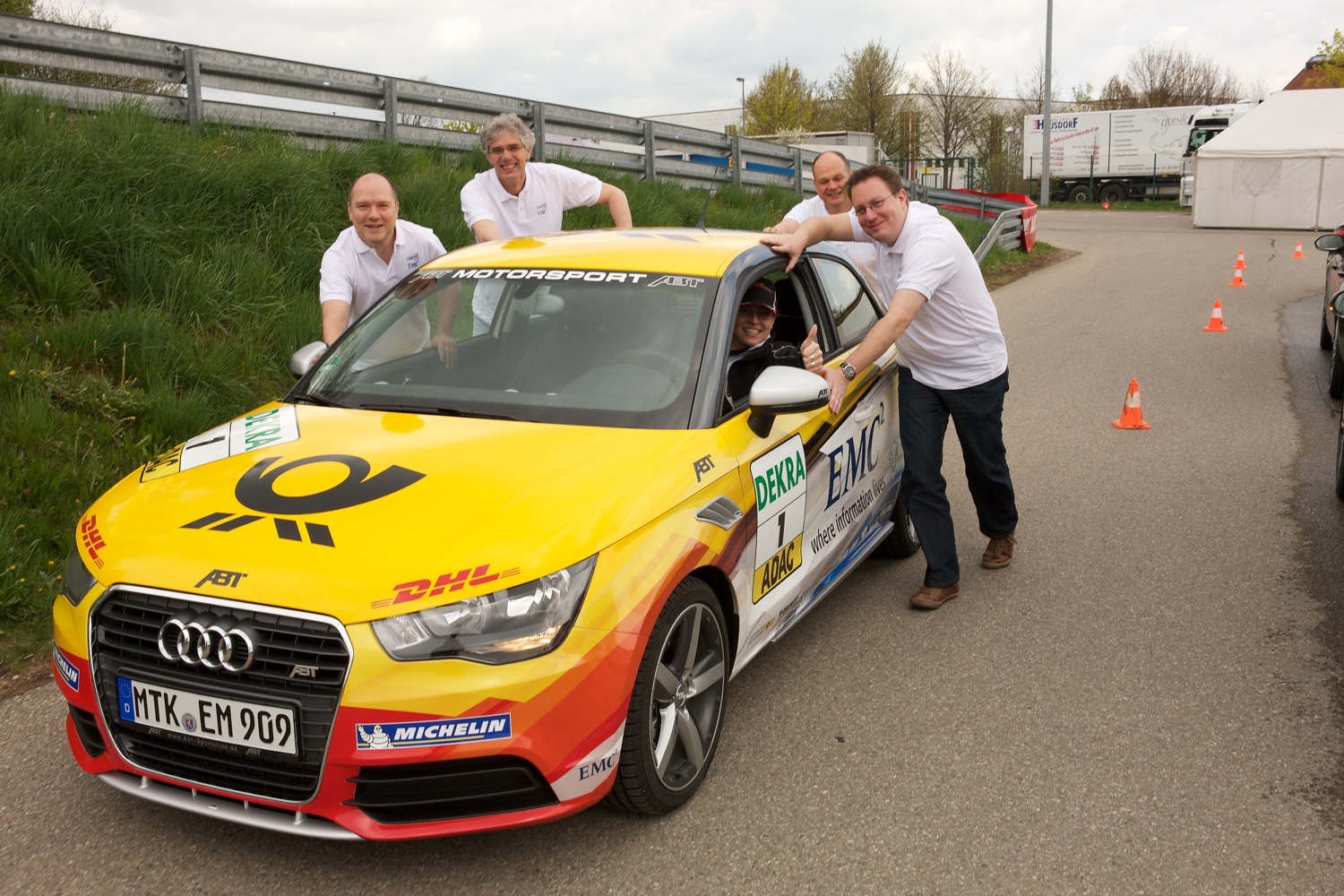 The EMC team gathers around a car at the Power and Speed Driving Experience